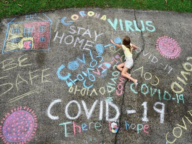 A young girl writes with chalk on her home driveway on the Gold Coast.